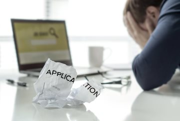 A ripped up piece of paper with the text Resume on it. There is a man in the background in business attire holding his head